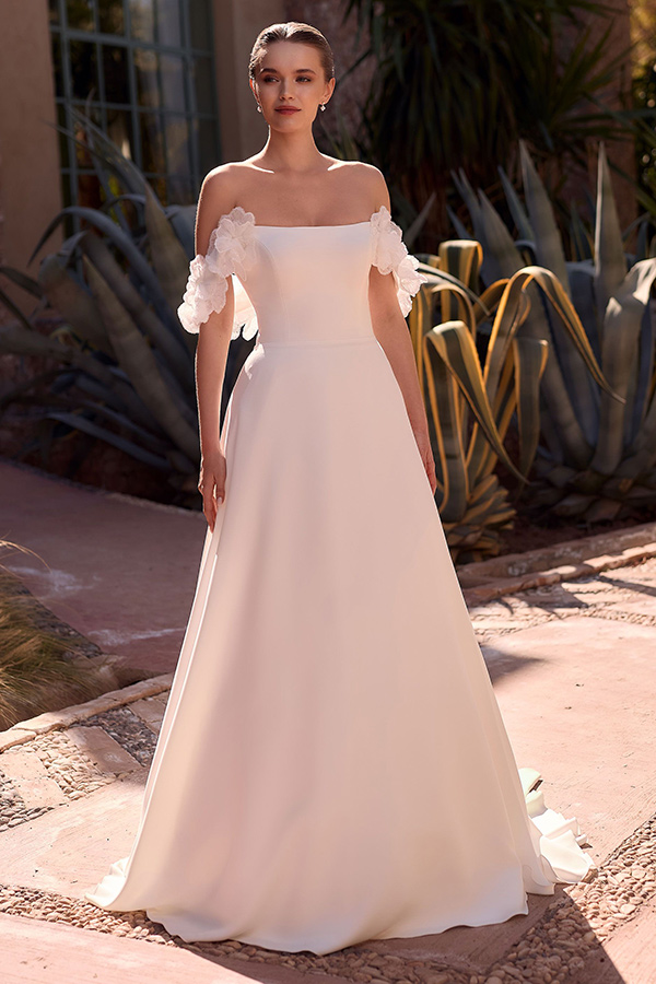 Junge Frau mit elegantem weißem Brautkleid und zarten Blumenärmeln vor Kakteen