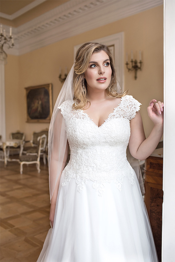 Junge Frau mit hellem Teint und blonden Haaren trägt ein elegantes weißes Brautkleid