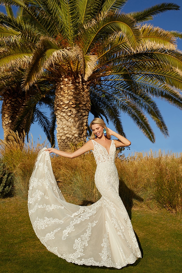 Eine blonde Frau im eleganten cremefarbenen Kleid lächelt fröhlich vor Palmen
