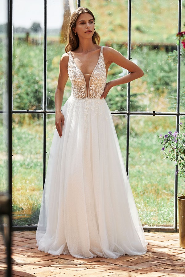 Eine Frau mit neutralem Gesichtsausdruck trägt ein weißes, elegantes Brautkleid