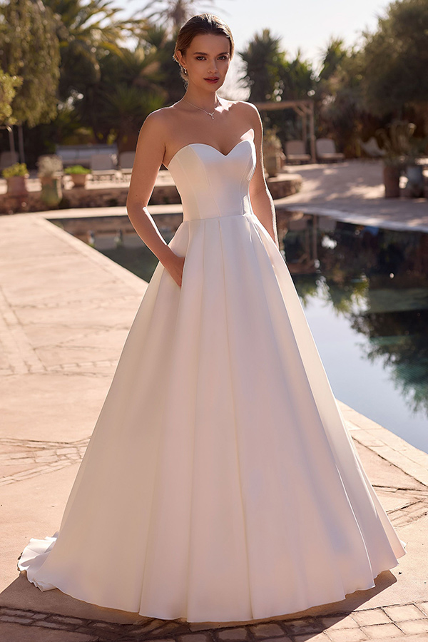 Eine junge Frau in einem eleganten weißen Brautkleid steht entspannt am Pool