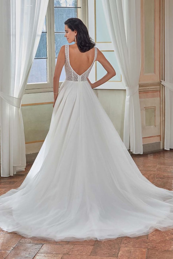 Eine Frau mit dunklen Haaren trägt ein elegantes weißes Brautkleid mit tiefem Rückenausschnitt