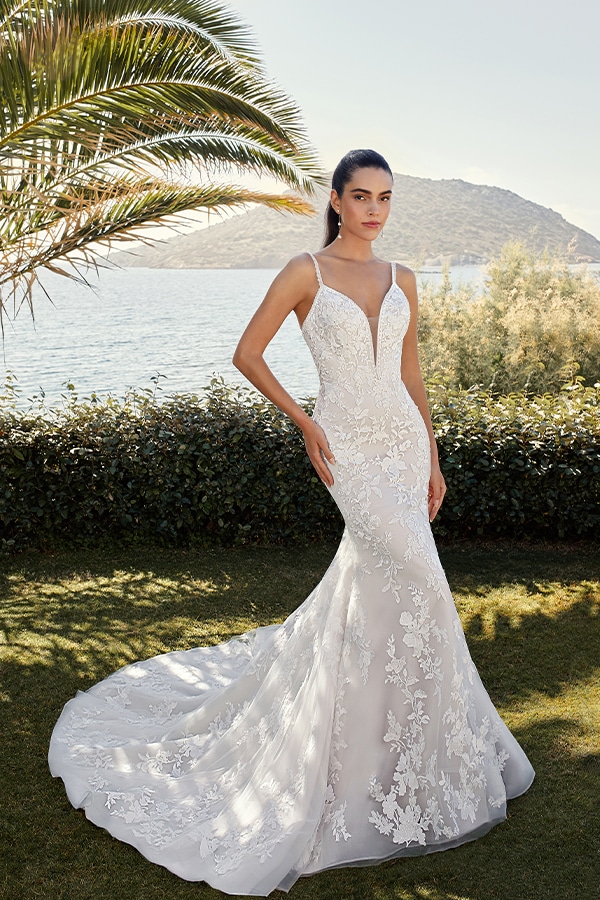 Eine junge Frau mit ernstem Blick trägt ein elegantes weißes Spitzenkleid am Meer