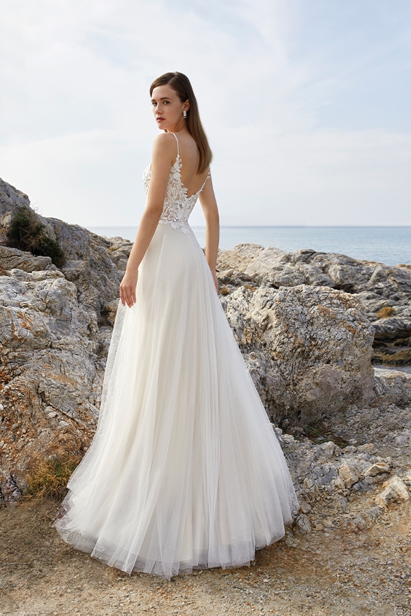 Junge Frau mit ernstem Blick im eleganten cremefarbenen Brautkleid am Felsenstrand