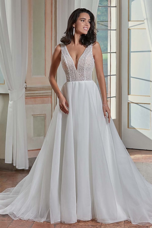 Junge Frau mit dunklem Haar im weißen Brautkleid lächelt in hellem Raum