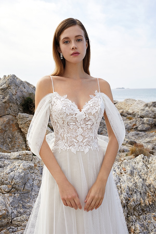 Junge Frau mit ernster Miene in weißem Spitzenkleid vor felsiger Meereskulisse