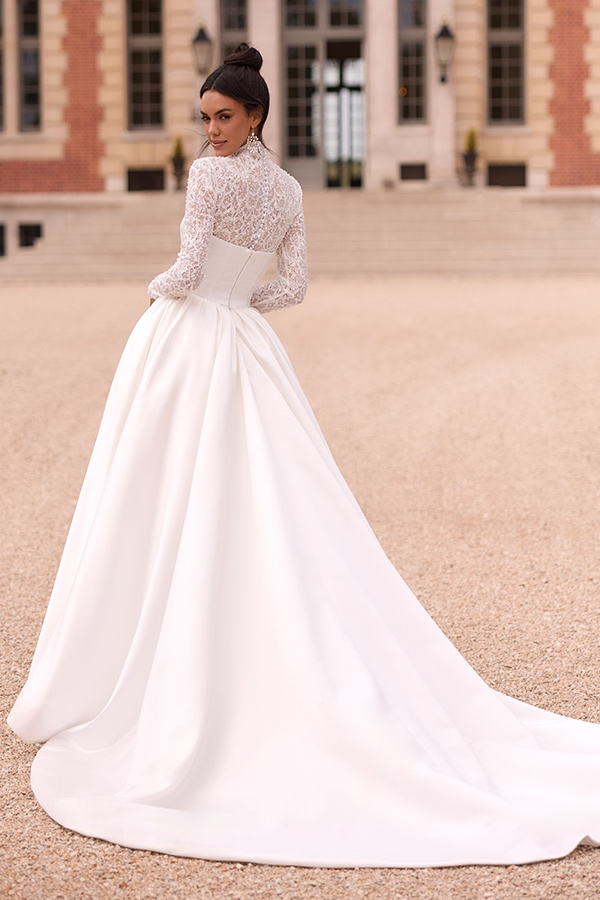 Eine Frau mit elegantem Dutt trägt ein weißes Brautkleid mit langer Schleppe und Spitzenärmeln