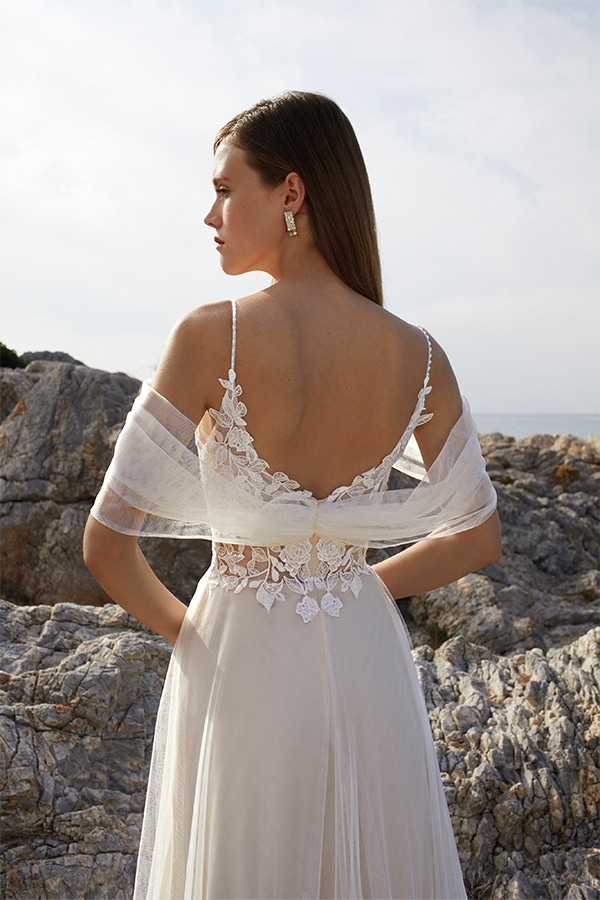 Eine junge Frau im cremefarbenen Spitzenkleid steht lächelnd vor Felsen im Freien