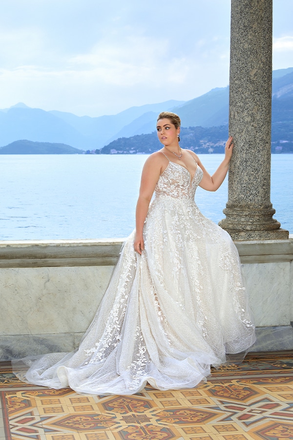 Frau mit ernstem Blick in weißem Spitzenkleid steht auf einer Terrasse am See