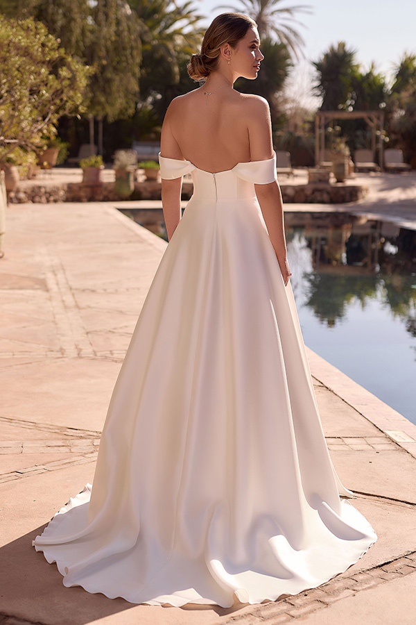 Eine Frau mit elegantem Dutt trägt ein schulterfreies weißes Kleid und steht am Pool