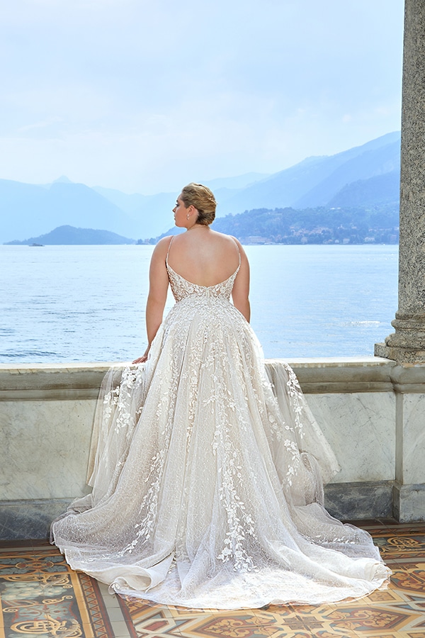 Eine Frau im eleganten cremefarbenen Brautkleid blickt auf einen ruhigen See