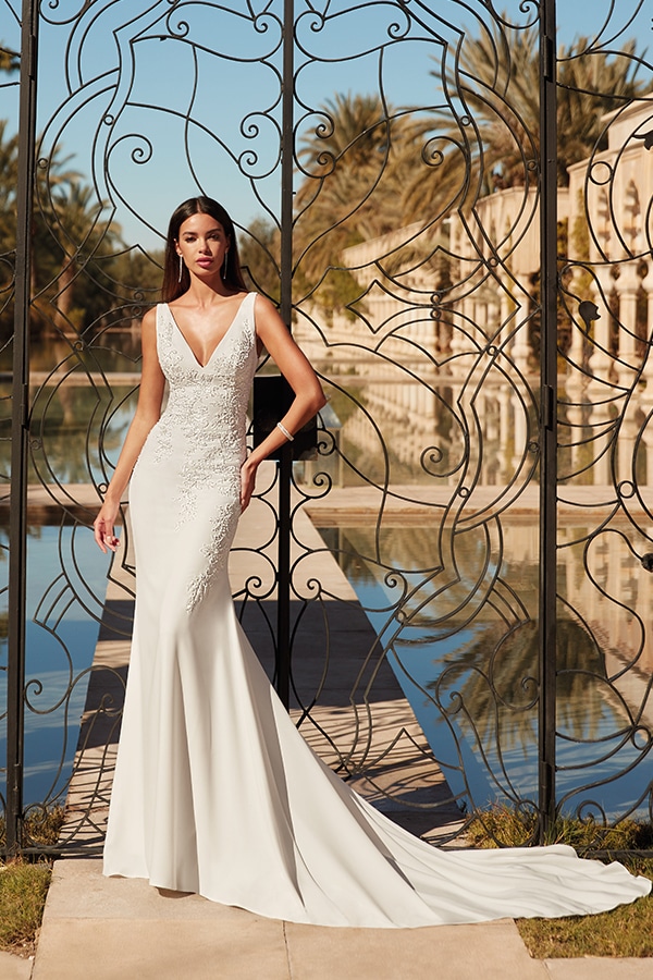 Eine junge Frau in elegantem weissem Brautkleid steht ernst vor schmiedeeisernem Tor