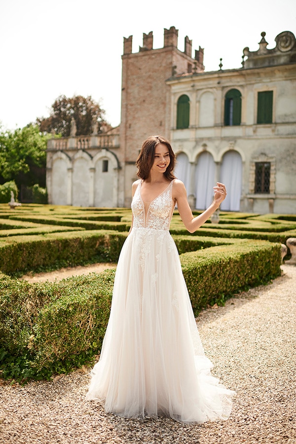 Eine lächelnde Frau mit braunen Haaren trägt ein weißes, elegantes Brautkleid im Garten