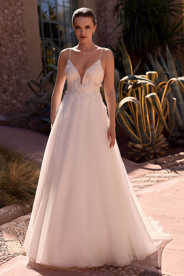 Eine junge Frau mit neutralem Blick trägt ein weißes Brautkleid mit Spitzeneinsatz