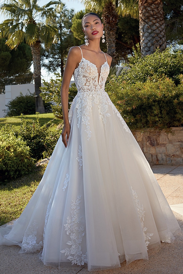 Eine elegante Frau mit ernstem Blick trägt ein weißes Spitzenbrautkleid im Garten