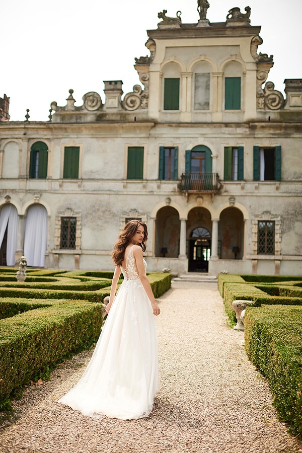 Eine lächelnde Frau im eleganten Brautkleid steht vor einer historischen Villa
