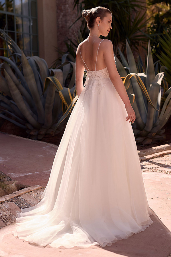 Eine junge Frau mit elegantem Dutt trägt ein weißes Brautkleid mit Spitzenrücken