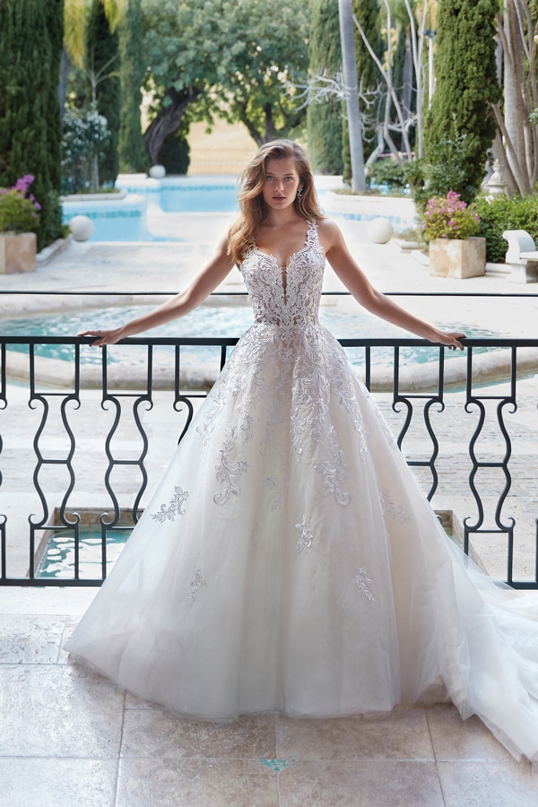 Junge Frau mit langen Haaren steht entspannt in weißem Spitzenkleid vor Pool