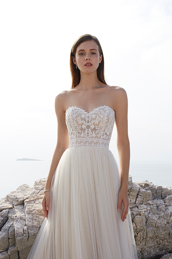 Junge Frau mit langen braunen Haaren trägt ein cremefarbenes Spitzenkleid und blickt ernst