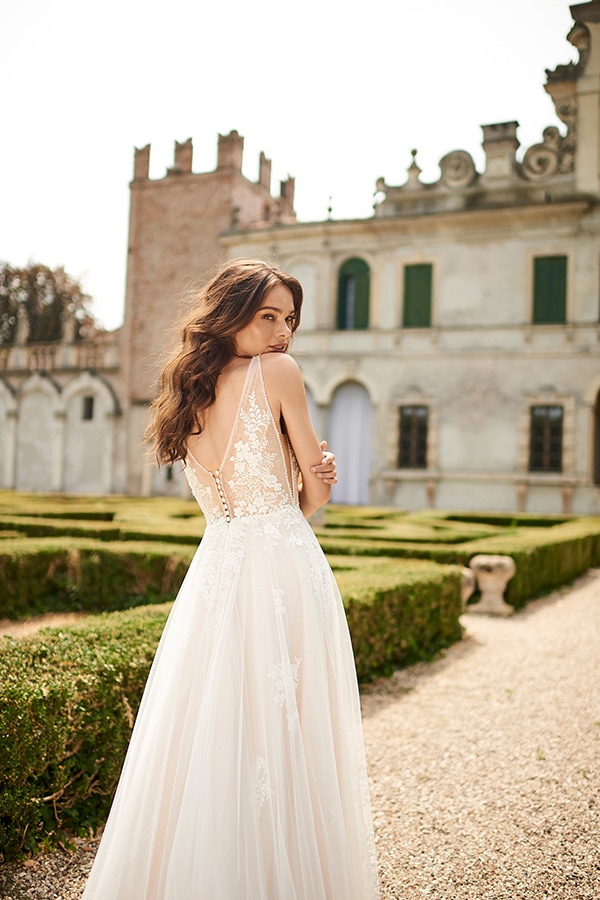 Eine junge Frau im weißen Spitzenkleid steht lächelnd im Garten vor einem Schloss