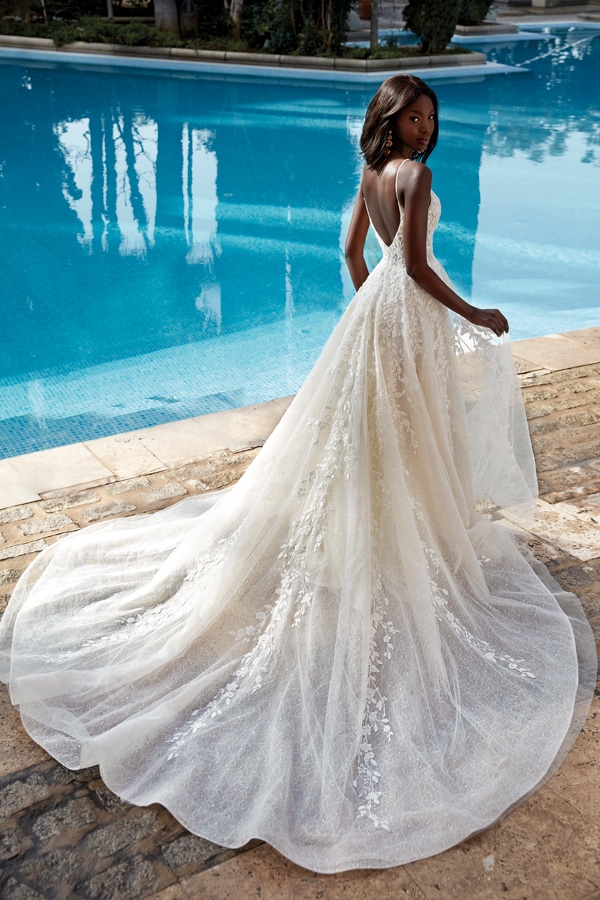 Eine elegant gekleidete Frau in weißem Spitzenkleid steht nachdenklich am Pool