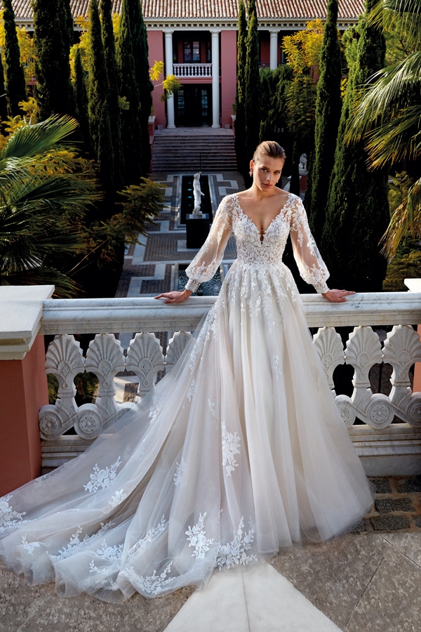 Eine blonde Frau mit ernster Miene trägt ein langes Spitzenbrautkleid mit Schleppe