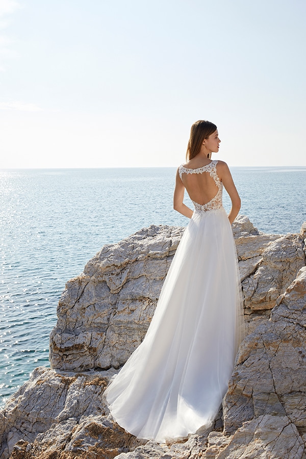 Eine Frau mit langen braunen Haaren steht im weißen Brautkleid auf Felsen am Meer