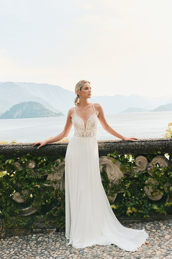 Eine blonde Frau im eleganten weißen Brautkleid blickt verträumt über einen See
