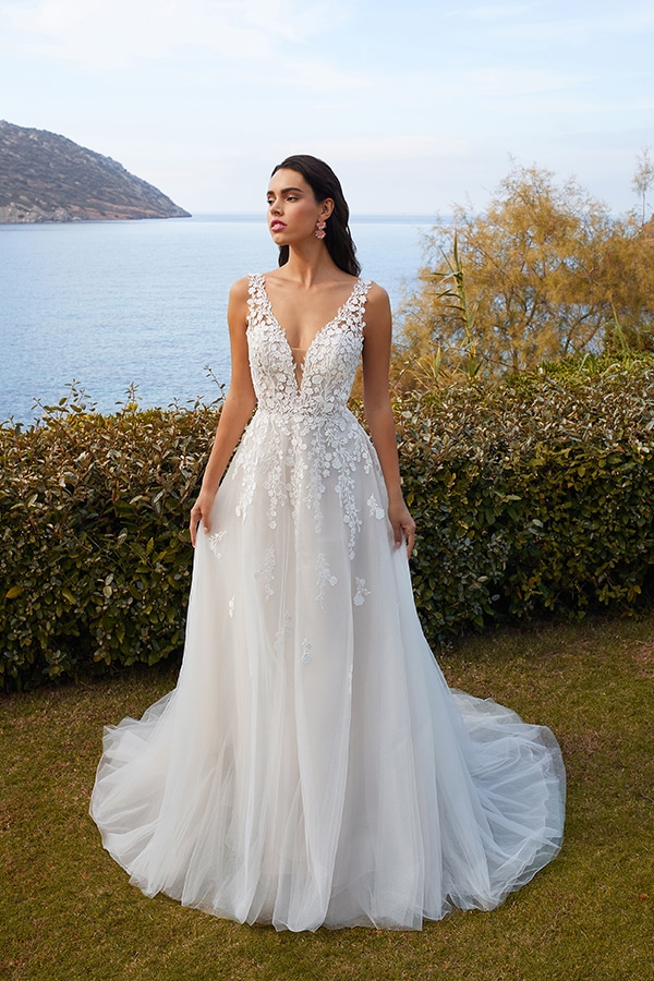 Eine Frau mit ernstem Blick trägt ein weißes, blumengeschmücktes Brautkleid am Meer