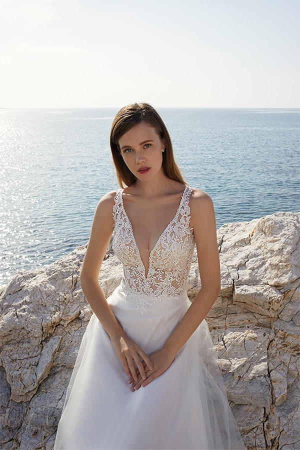 Junge Frau mit langen braunen Haaren und cremeweißem Spitzenkleid vor dem Meer