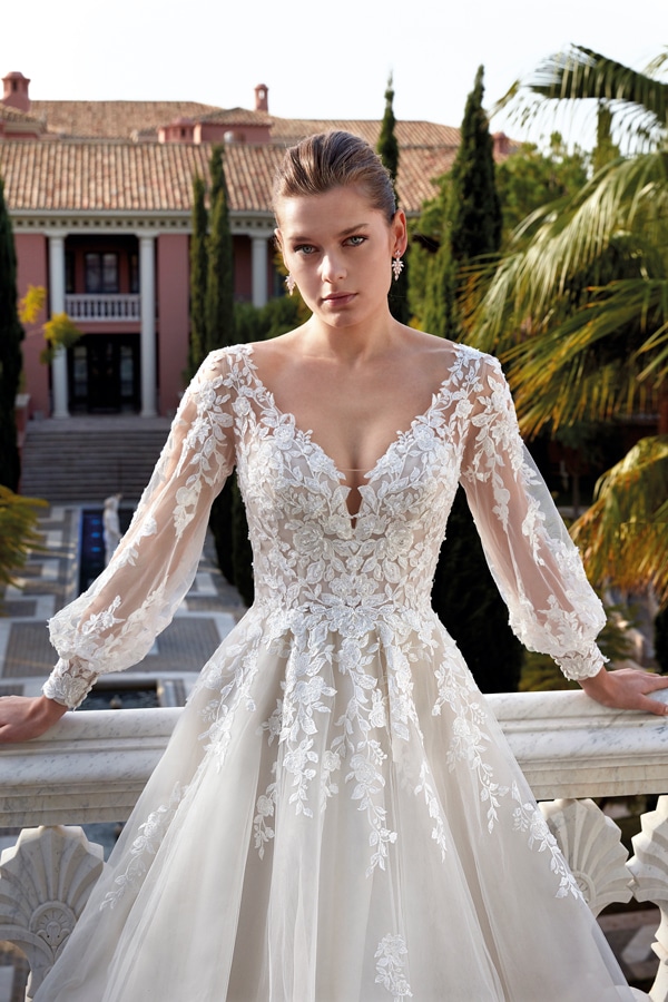 Junge Frau mit ernster Miene in weißem Spitzenkleid vor mediterraner Villa