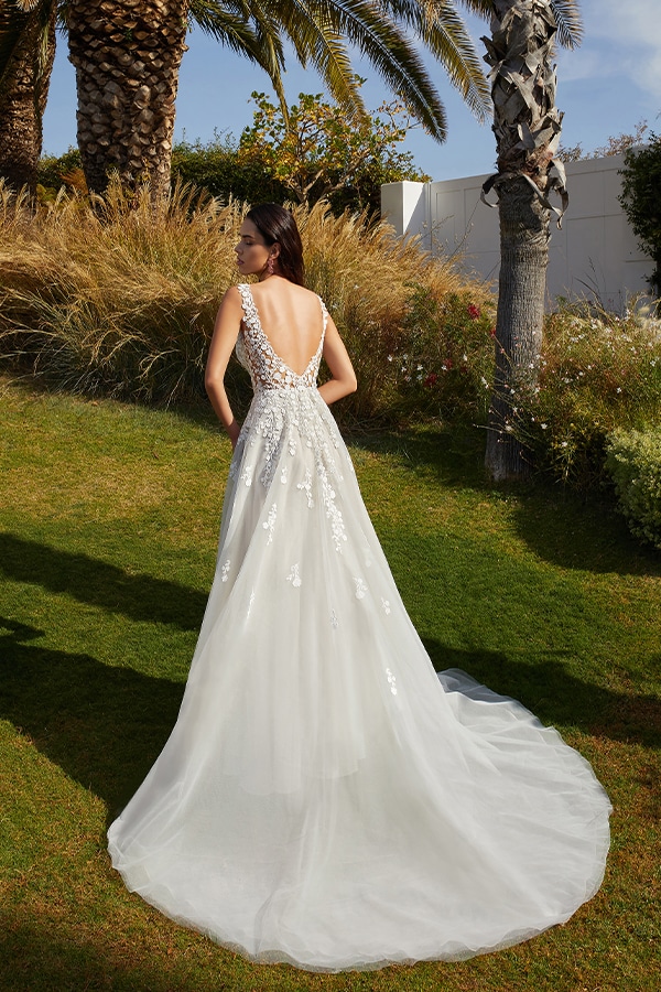 Eine Frau mit langen dunklen Haaren trägt ein weißes Brautkleid mit tiefem Rückenausschnitt im Garten