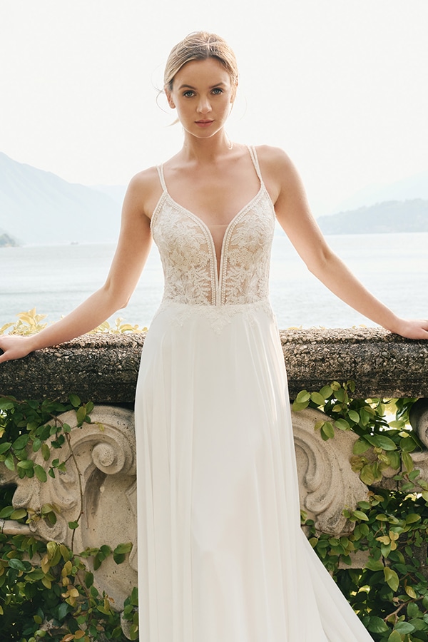 Junge Frau mit neutralem Gesichtsausdruck im eleganten weißen Spitzenkleid vor See