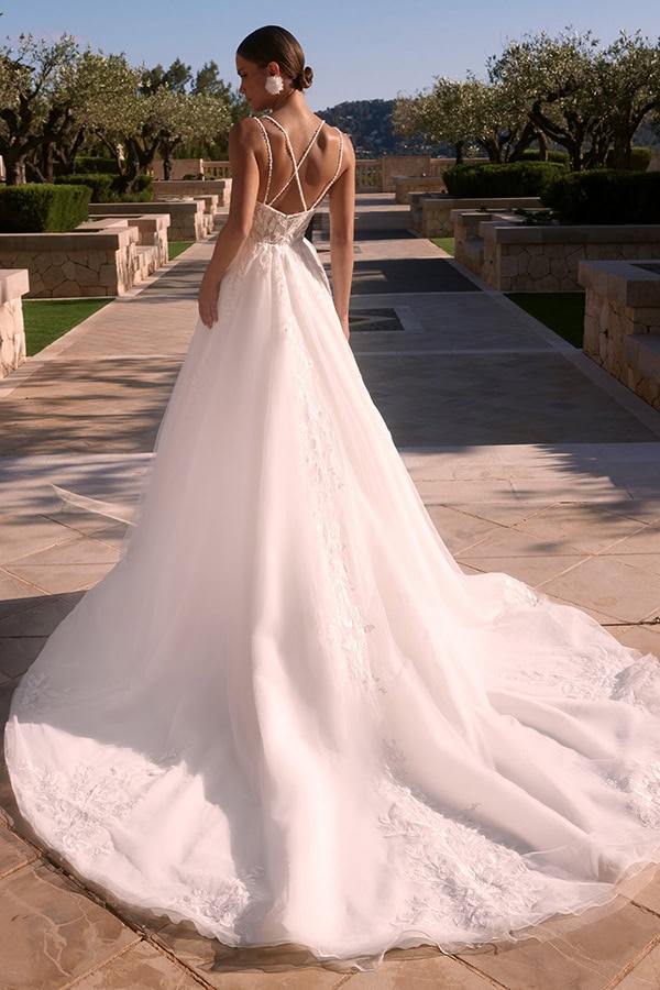 Eine Frau im weißen Brautkleid mit Spitzendetails steht auf einem sonnigen Steinweg