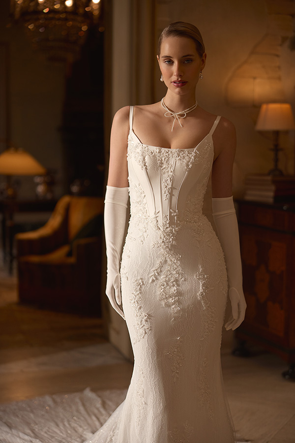 Eine elegante Frau im weißen Hochzeitskleid lächelt dezent und trägt Handschuhe