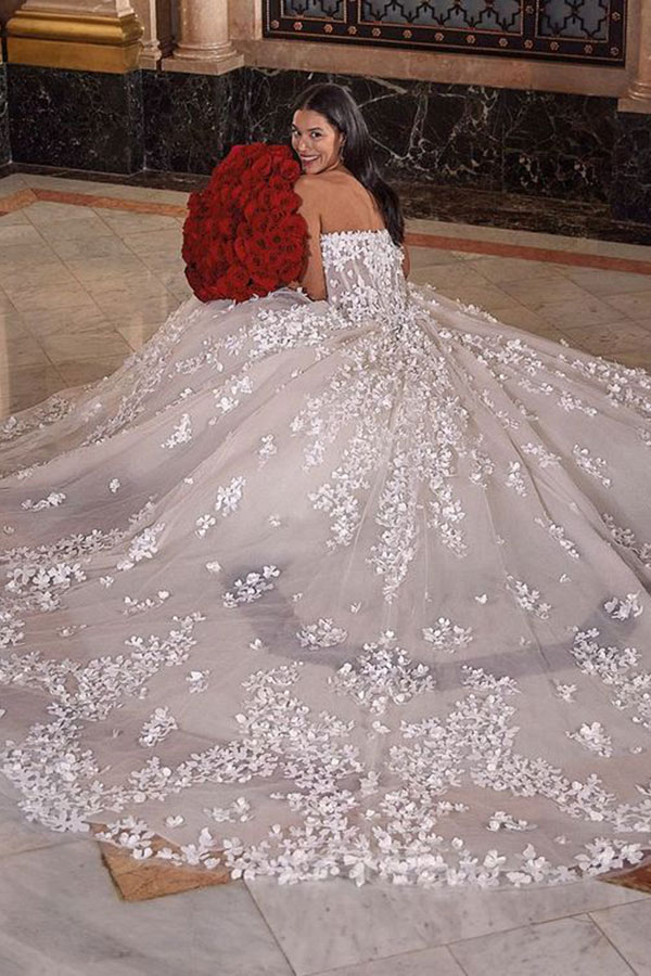 Eine junge Frau lächelt glücklich in einem weißen Blumen Kleid mit roten Rosen in der Hand