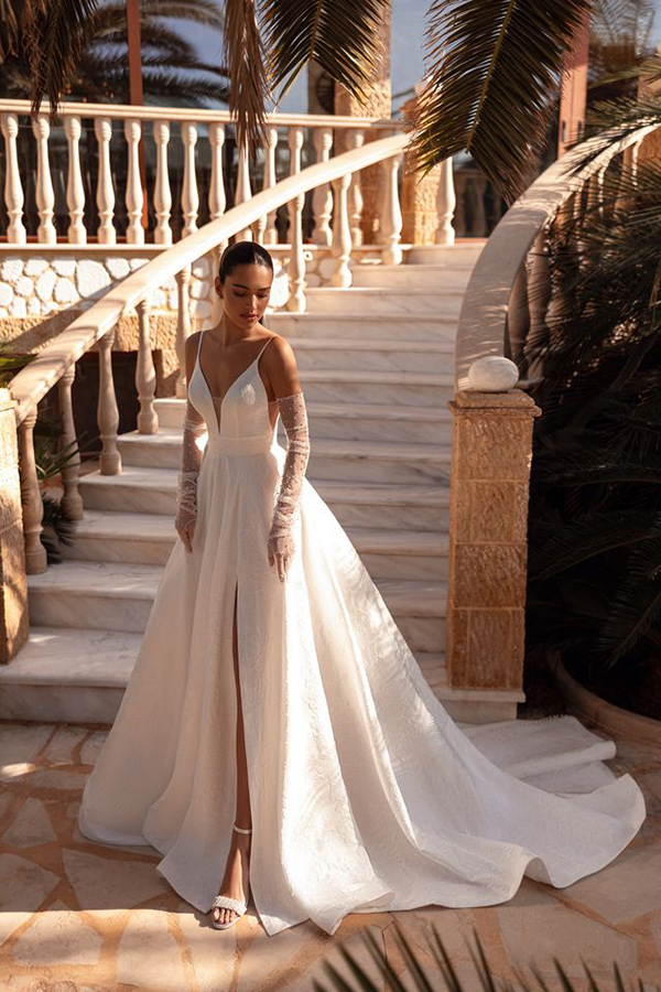 Eine elegant gekleidete Frau im weißen Brautkleid steht verträumt auf einer Steintreppe