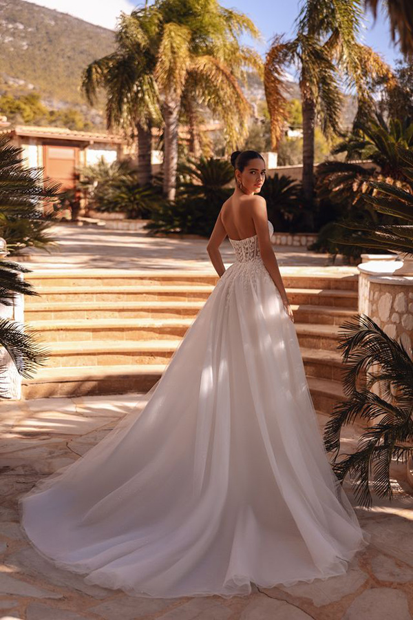 Eine Frau im weißen Brautkleid blickt ernst über die Schulter und steht vor Palmen