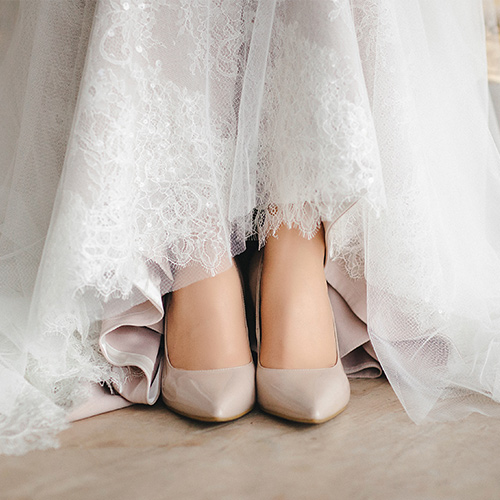 Eine Frau im weißen Spitzenkleid zeigt elegante beigefarbene Schuhe unter dem Saum
