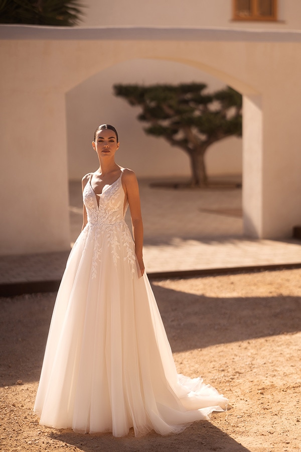 Eine Frau mit ernstem Blick steht draußen im Sonnenlicht in einem weißen Brautkleid