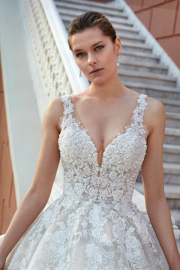 Eine junge Frau mit ernster Miene trägt ein elegantes weißes Spitzenkleid vor einer Treppe