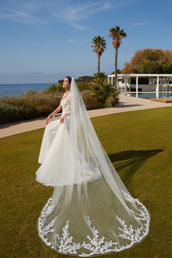 Eine Braut mit ernstem Blick trägt ein langes weißes Kleid und steht im Sonnenschein