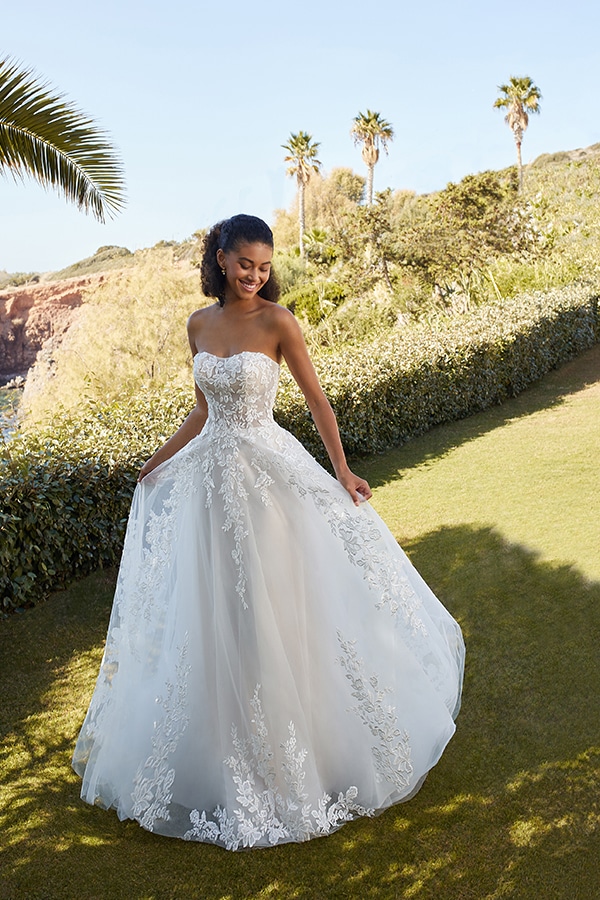 Junge Frau mit lockigem Haar lacht strahlend im weißen Spitzen-Brautkleid im Garten