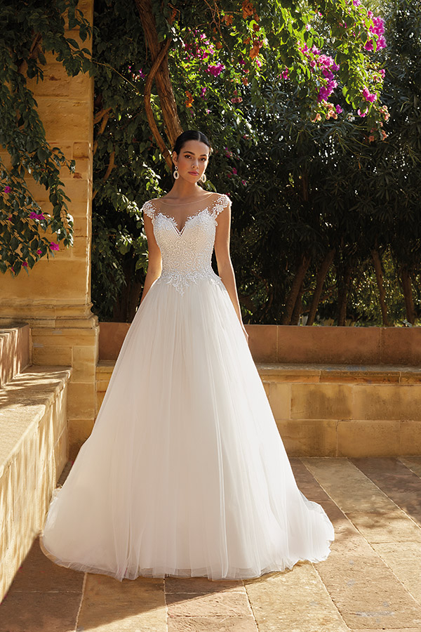 Eine junge Frau mit ernstem Blick trägt ein elegantes weißes Spitzenkleid im Garten