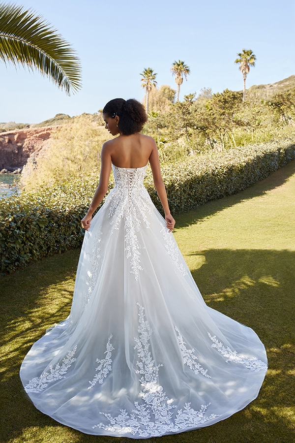 Eine lächelnde Frau im weißen Spitzenkleid steht im Garten mit Palmen und Sonne