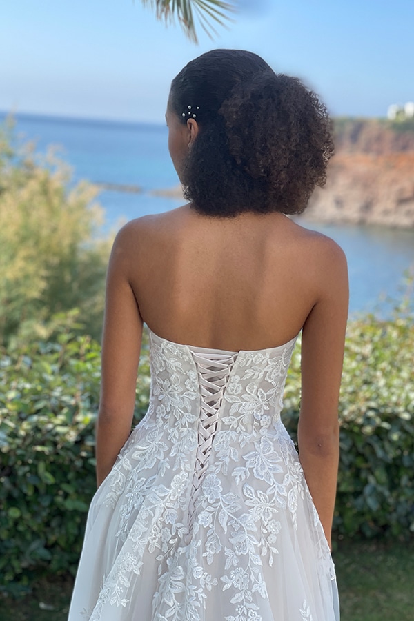 Eine Frau mit lockigem, dunklem Haar trägt ein weißes Spitzenkleid und blickt aufs Meer