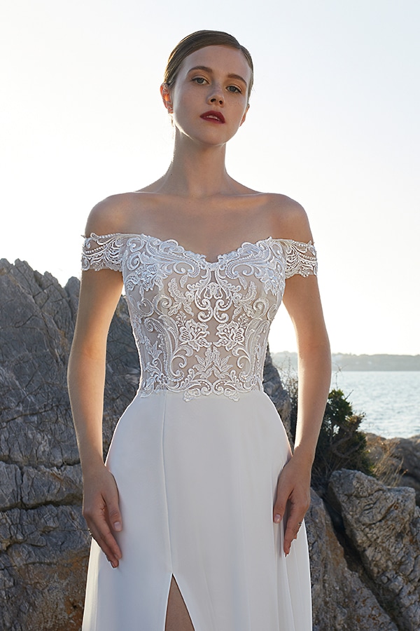 Junge Frau mit ernstem Blick in weißem Spitzenkleid vor Felsen am Meer