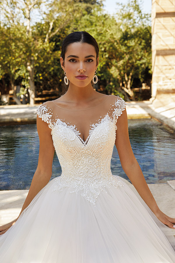 Junge Frau mit ernstem Blick trägt ein weißes, detailreich verziertes Brautkleid