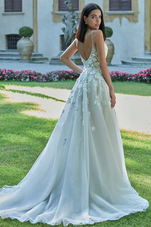 Eine junge Frau mit dunklem Haar trägt ein weißes Spitzenkleid und schaut ernst zurück