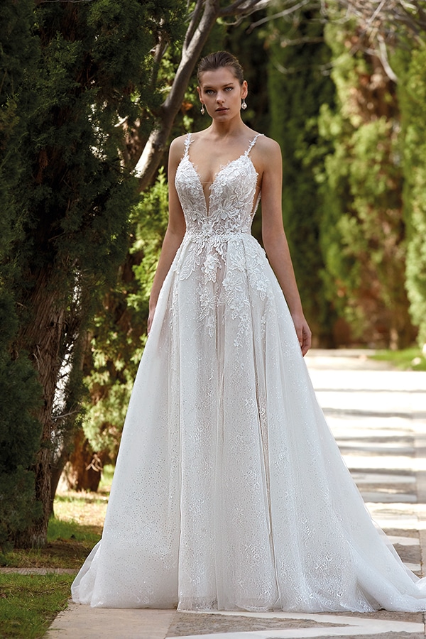 Eine junge Frau steht ernst in einem eleganten weißen Spitzenkleid im Gartenweg
